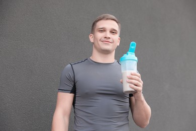 Athletic man with shaker of protein drink near grey wall