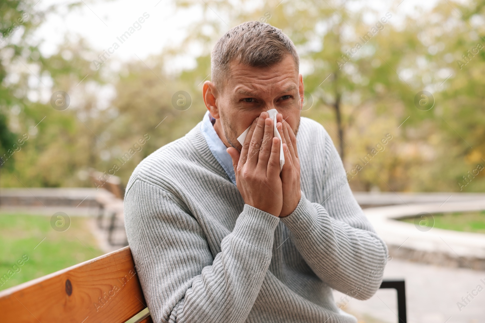 Photo of Man with tissue blowing runny nose in park