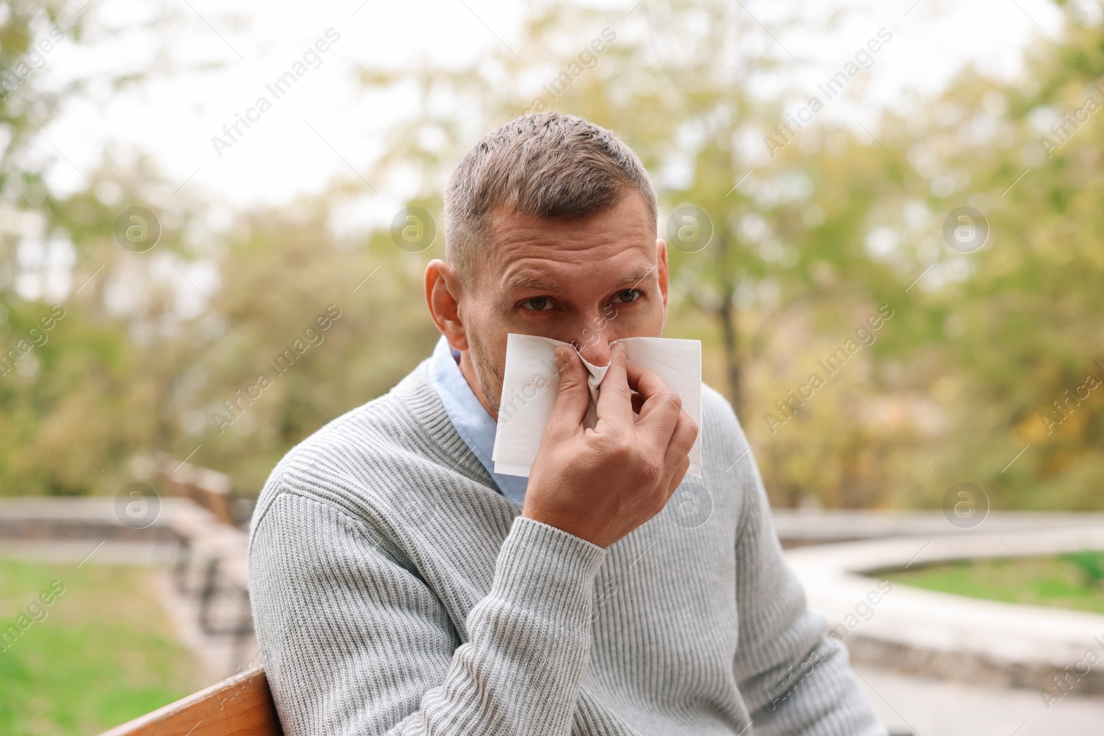 Photo of Man with tissue blowing runny nose in park