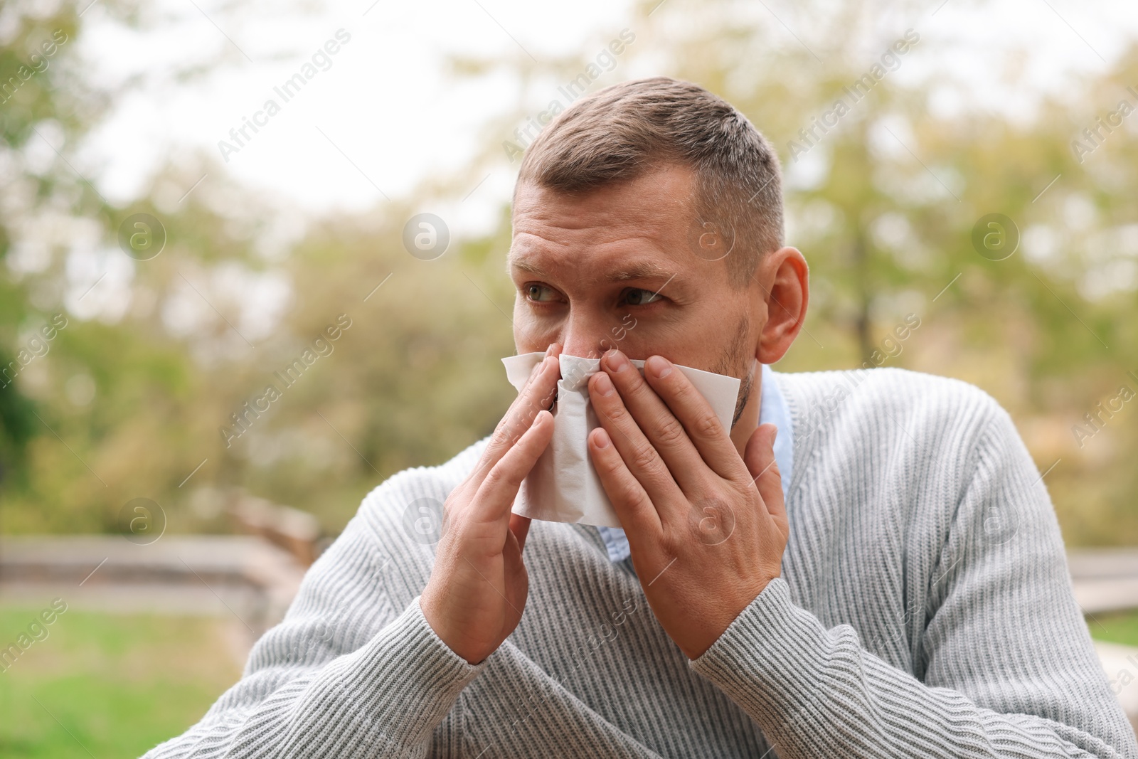 Photo of Man with tissue blowing runny nose in park