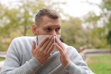 Man with tissue blowing runny nose in park