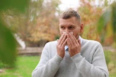 Photo of Man with tissue blowing runny nose in park