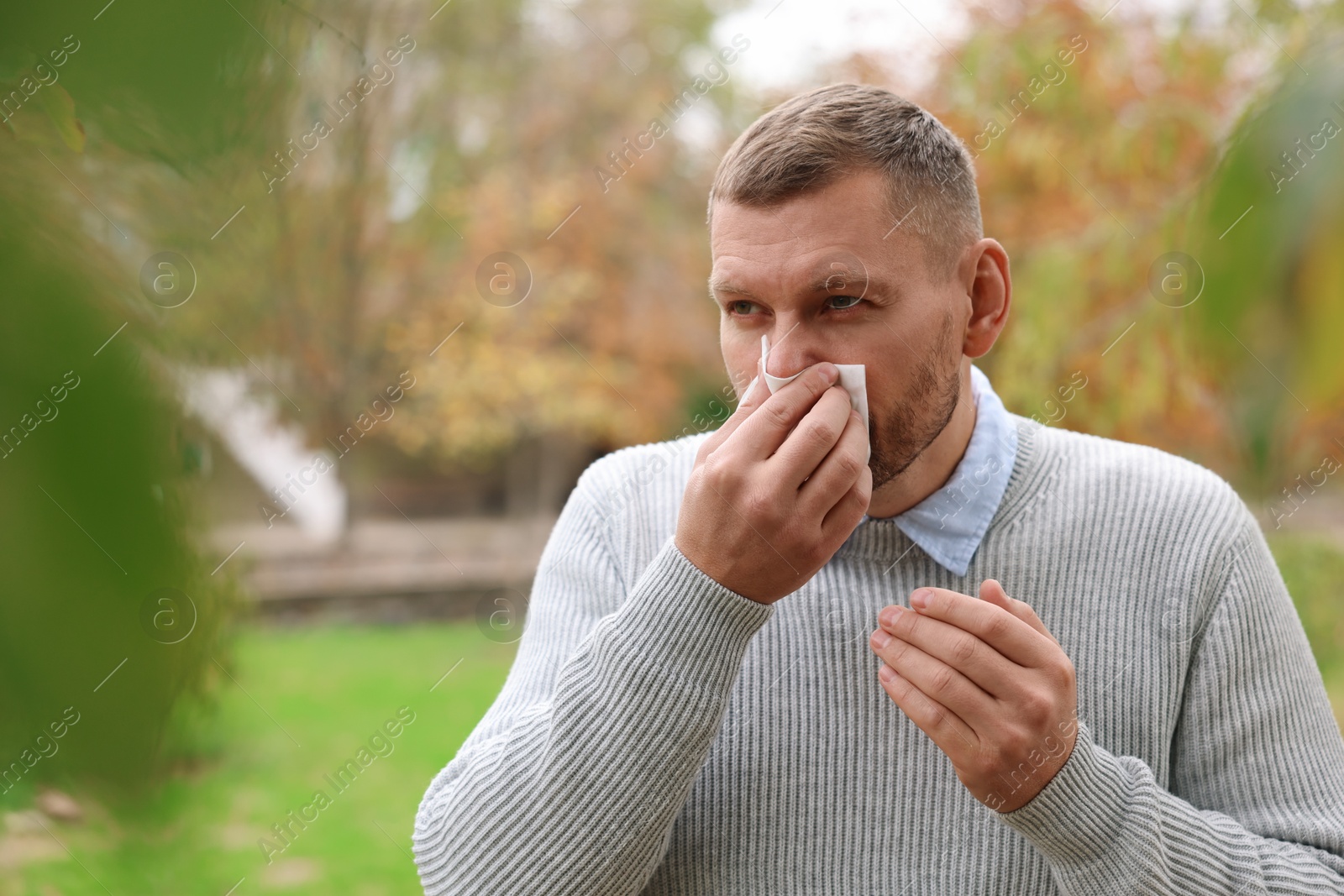 Photo of Man with tissue blowing runny nose in park