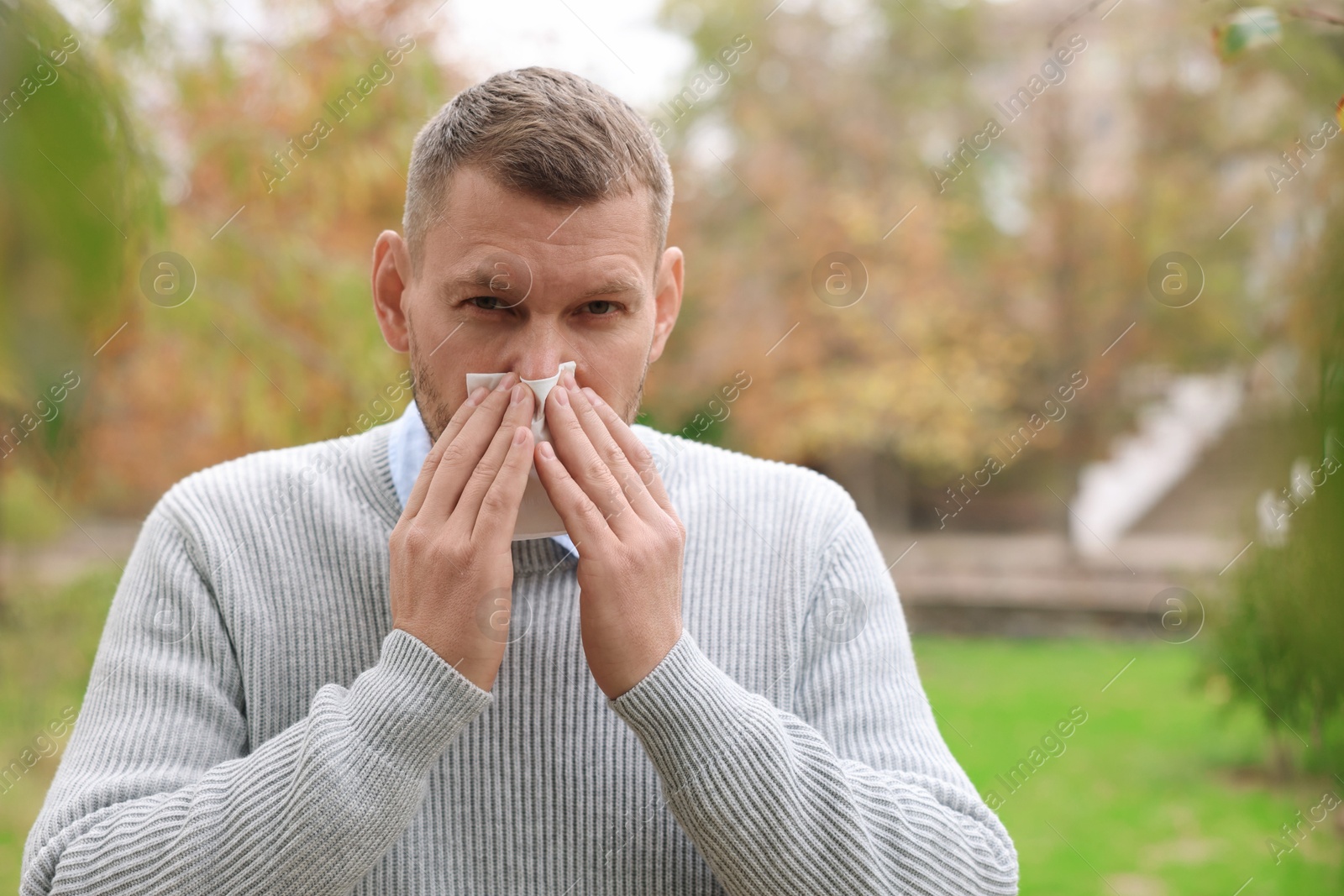 Photo of Man with tissue blowing runny nose in park