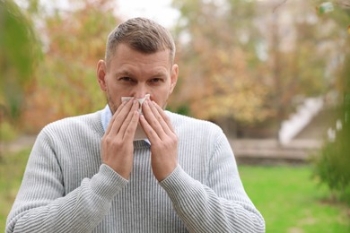 Man with tissue blowing runny nose in park