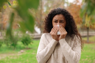 Photo of Young woman with runny nose in park. Space for text