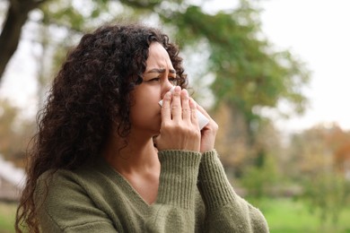 Photo of Young woman with runny nose in park. Space for text