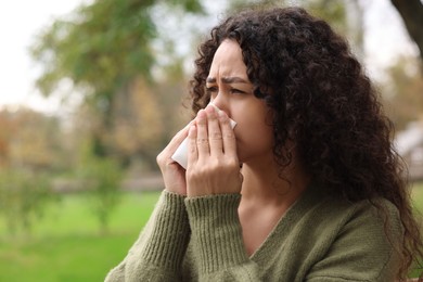 Photo of Young woman with runny nose in park. Space for text