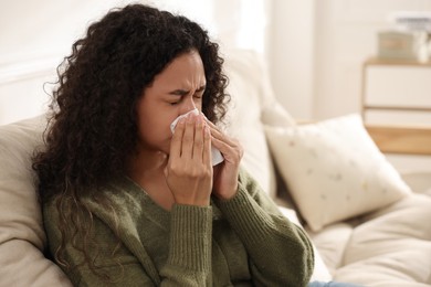 Photo of Young woman with tissue blowing runny nose at home