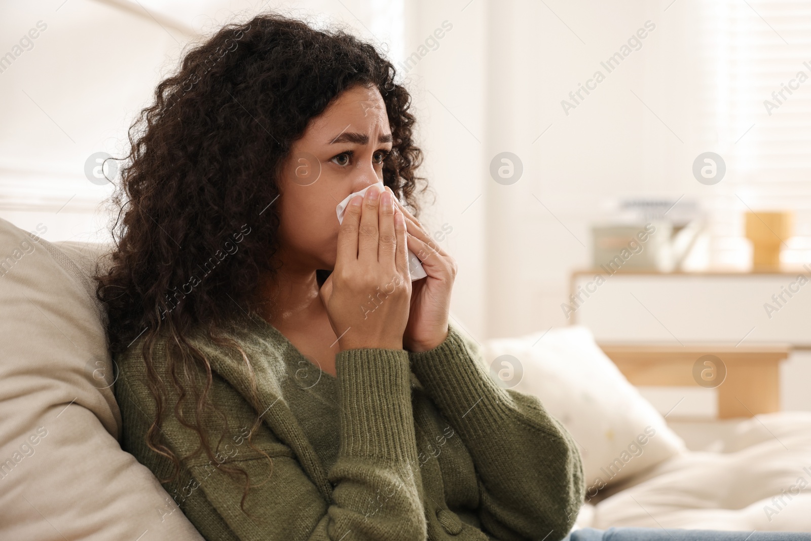 Photo of Young woman with tissue blowing runny nose at home. Space for text