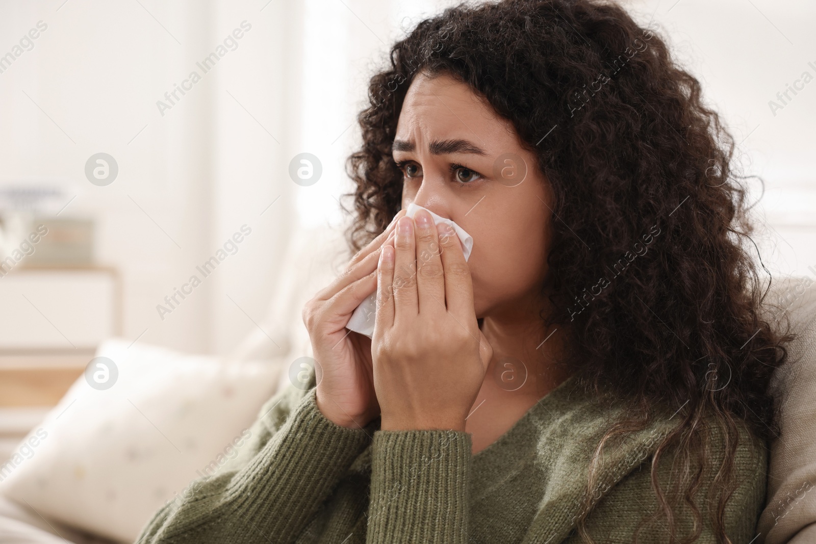 Photo of Young woman with tissue blowing runny nose at home