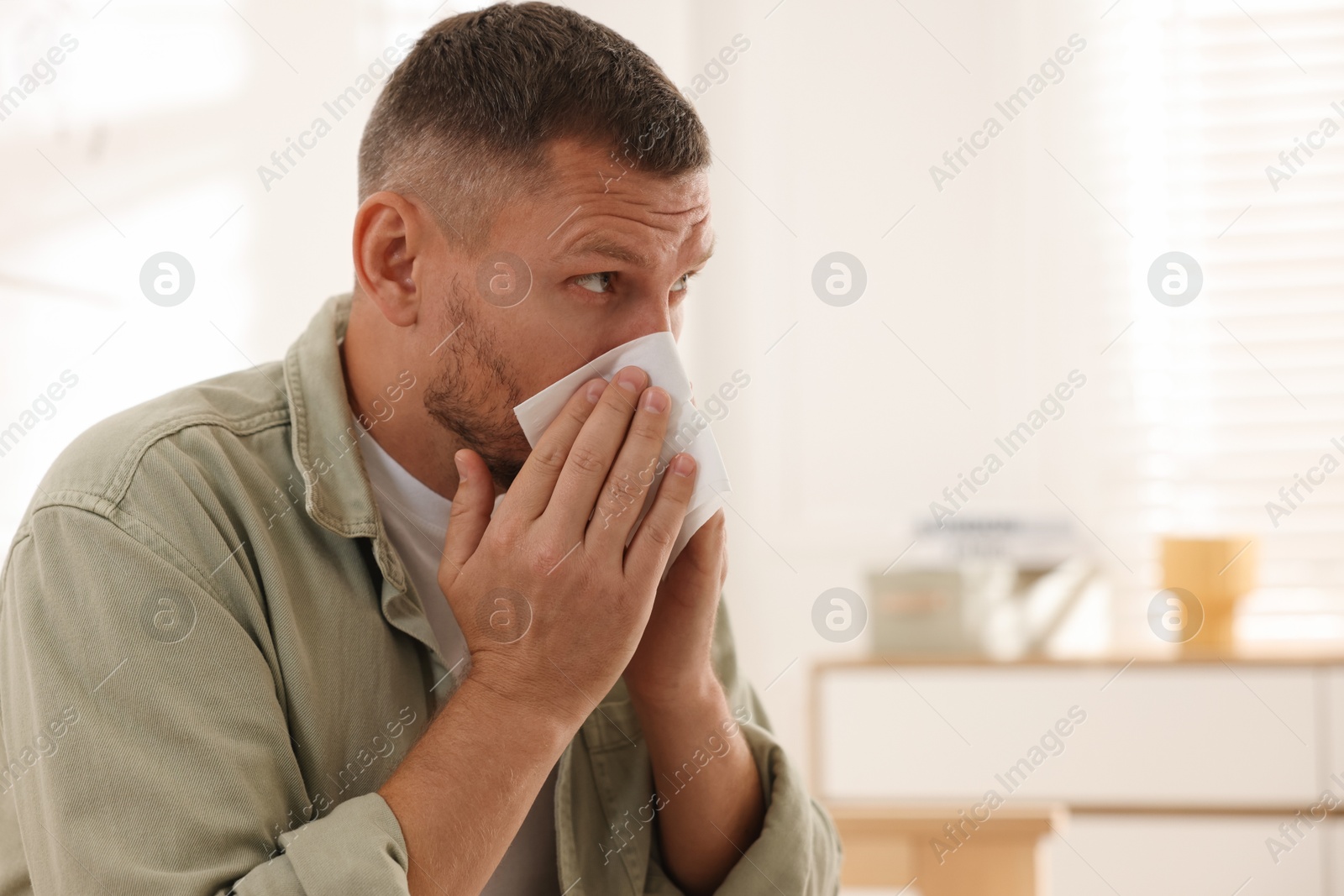 Photo of Man with tissue blowing runny nose at home. Space for text