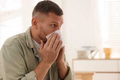 Man with tissue blowing runny nose at home. Space for text