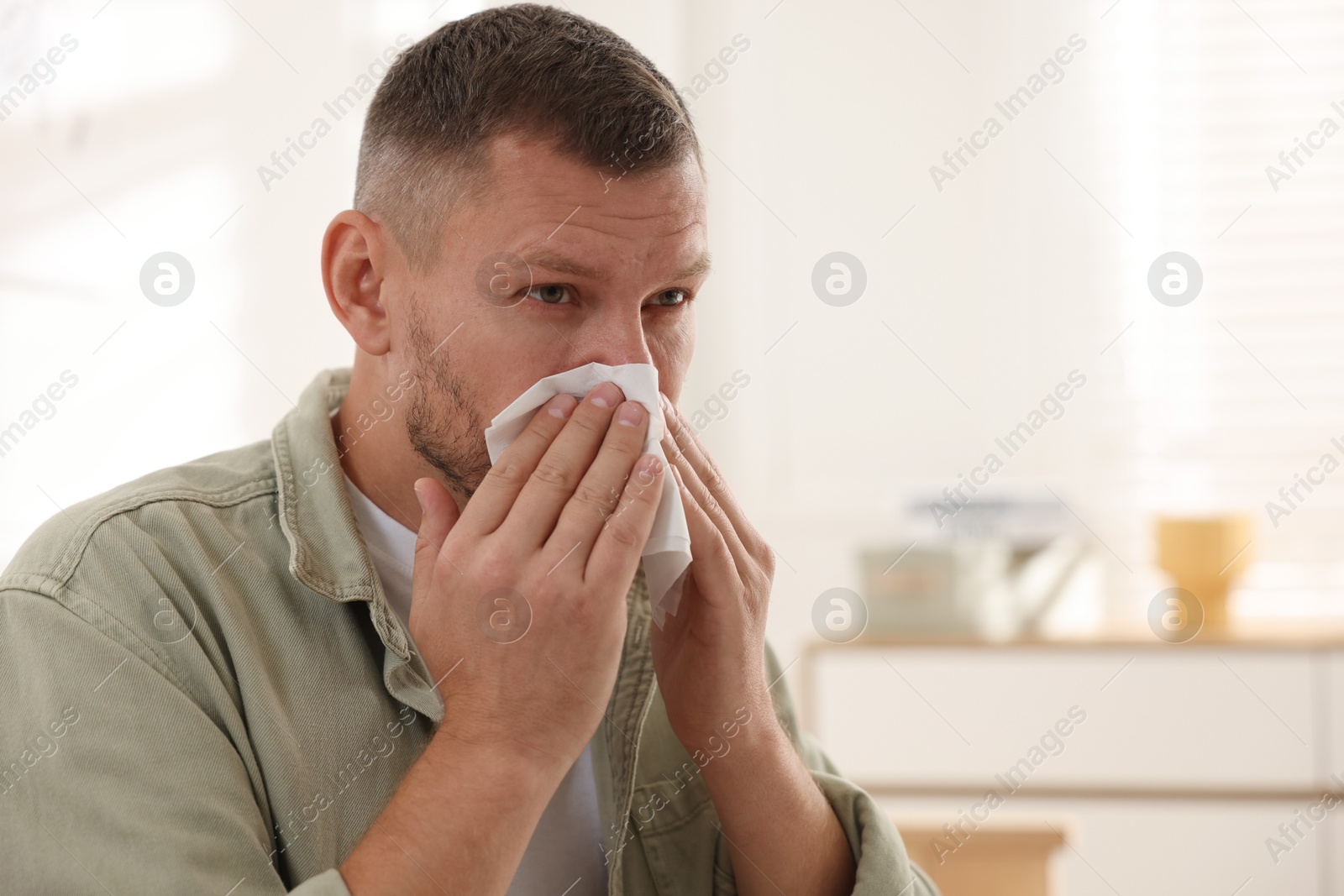 Photo of Man with tissue blowing runny nose at home. Space for text