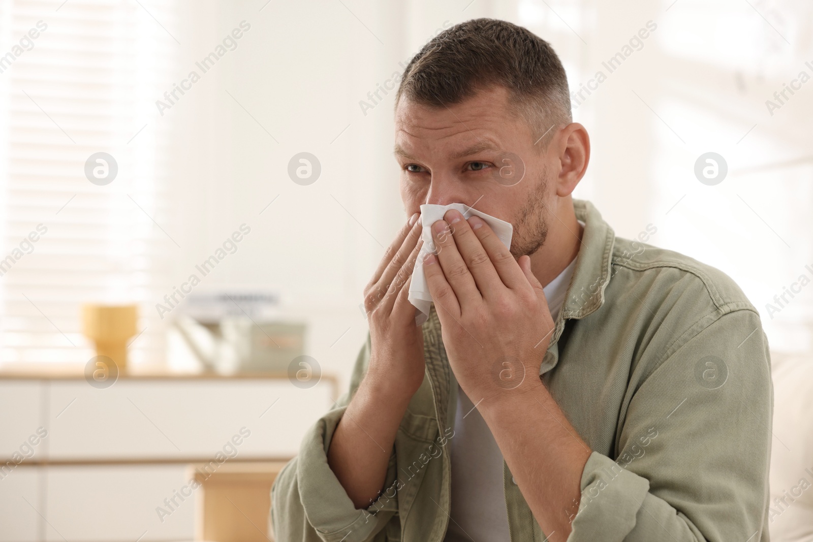 Photo of Man with tissue blowing runny nose at home. Space for text