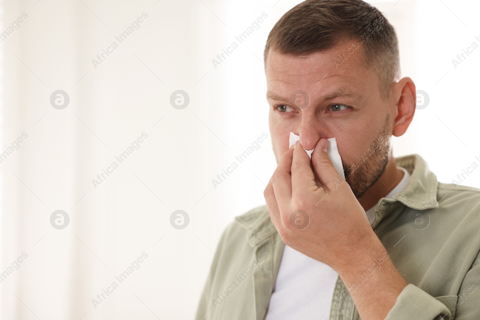 Photo of Man with tissue blowing runny nose at home. Space for text