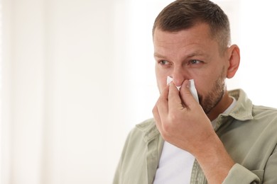 Photo of Man with tissue blowing runny nose at home. Space for text