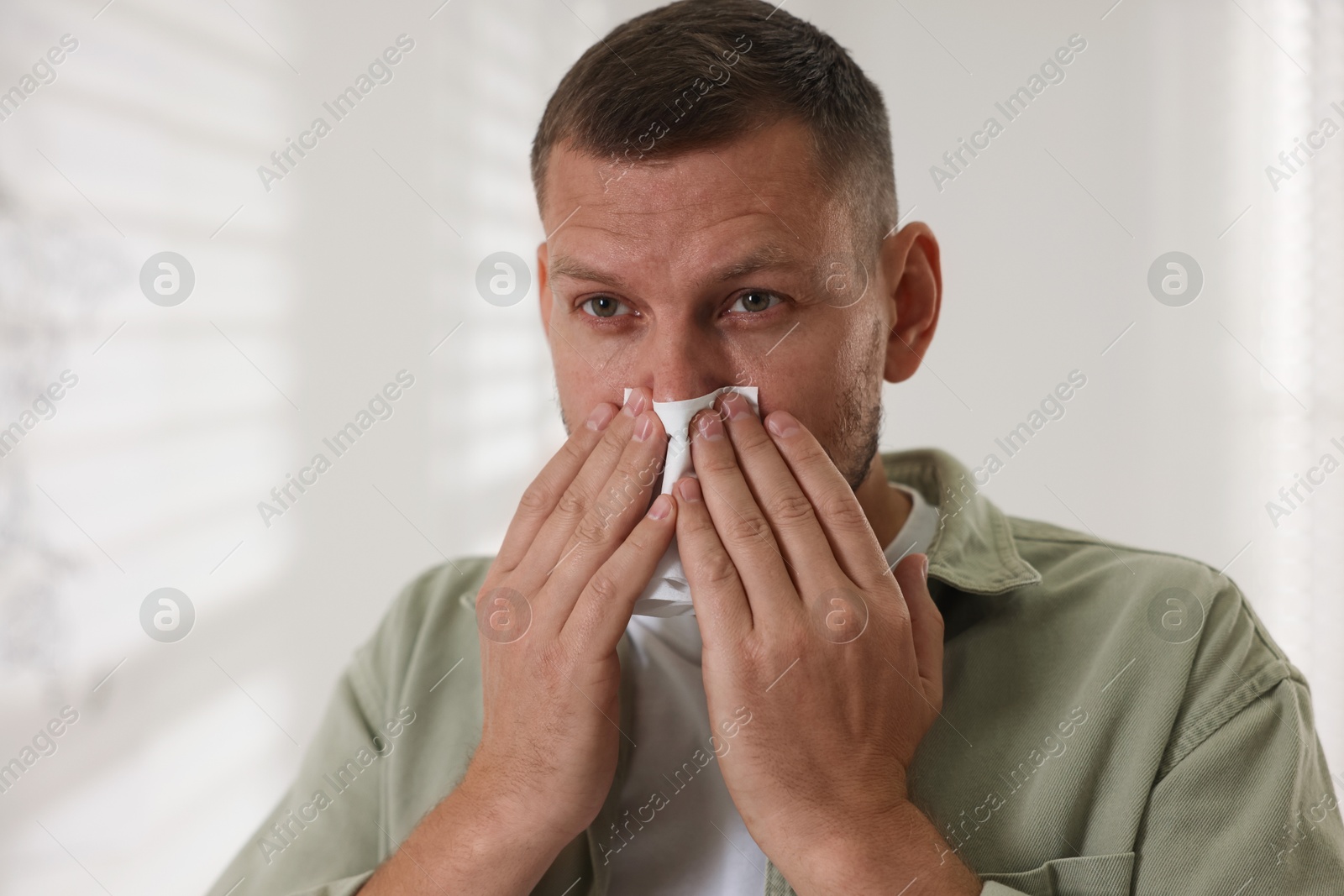 Photo of Man with tissue blowing runny nose at home