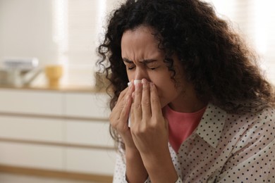 Photo of Young woman with tissue blowing runny nose at home