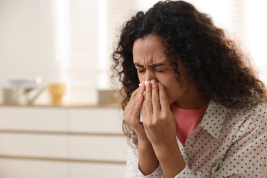 Photo of Young woman with tissue blowing runny nose at home