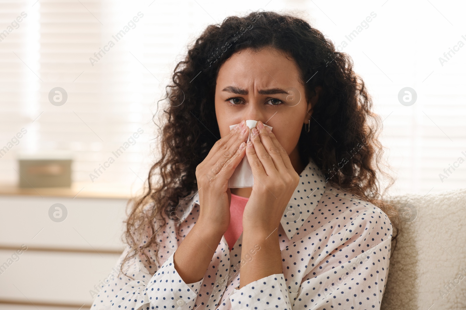 Photo of Young woman with tissue blowing runny nose at home