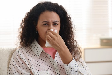 Photo of Young woman with tissue blowing runny nose at home