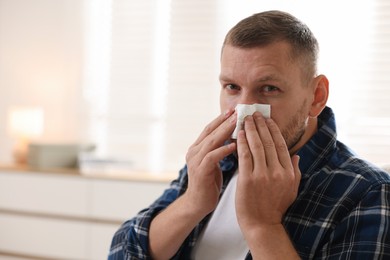 Photo of Man with tissue blowing runny nose at home. Space for text