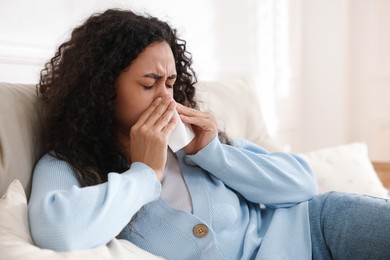 Photo of Young woman with tissue blowing runny nose at home