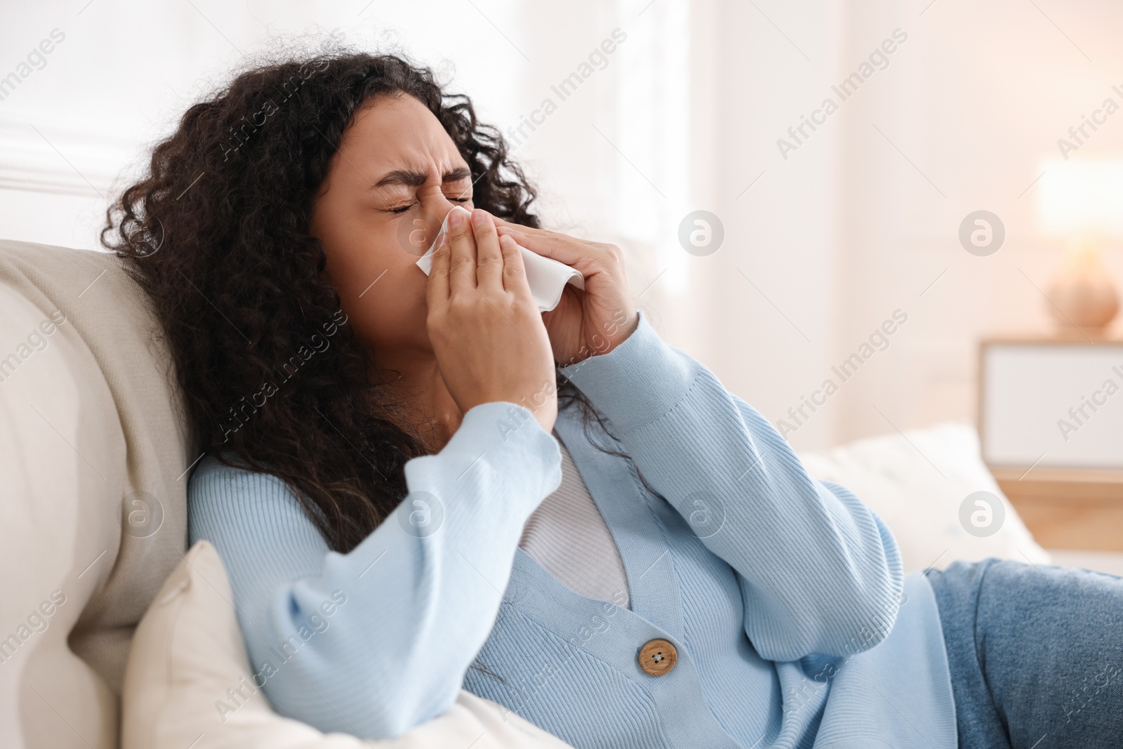 Photo of Young woman with tissue blowing runny nose at home