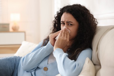 Photo of Young woman with tissue blowing runny nose at home