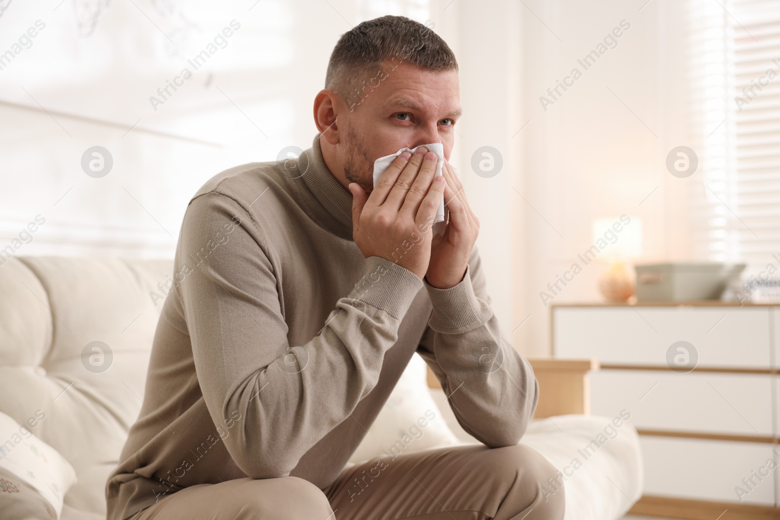 Photo of Man with tissue blowing runny nose at home