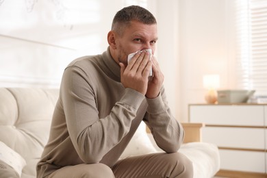 Photo of Man with tissue blowing runny nose at home