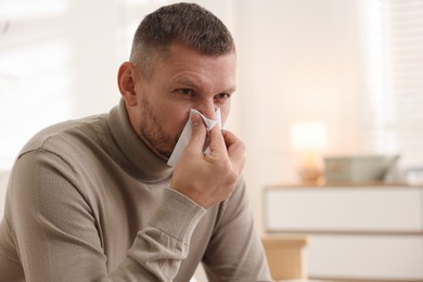 Photo of Man with tissue blowing runny nose at home. Space for text