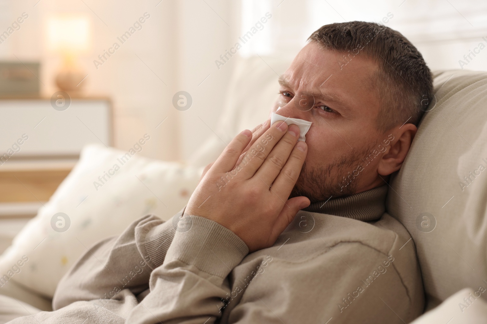 Photo of Man with tissue blowing runny nose at home. Space for text