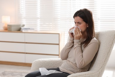 Photo of Young woman with tissue blowing runny nose at home. Space for text