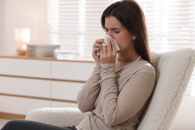 Photo of Young woman with tissue blowing runny nose at home. Space for text