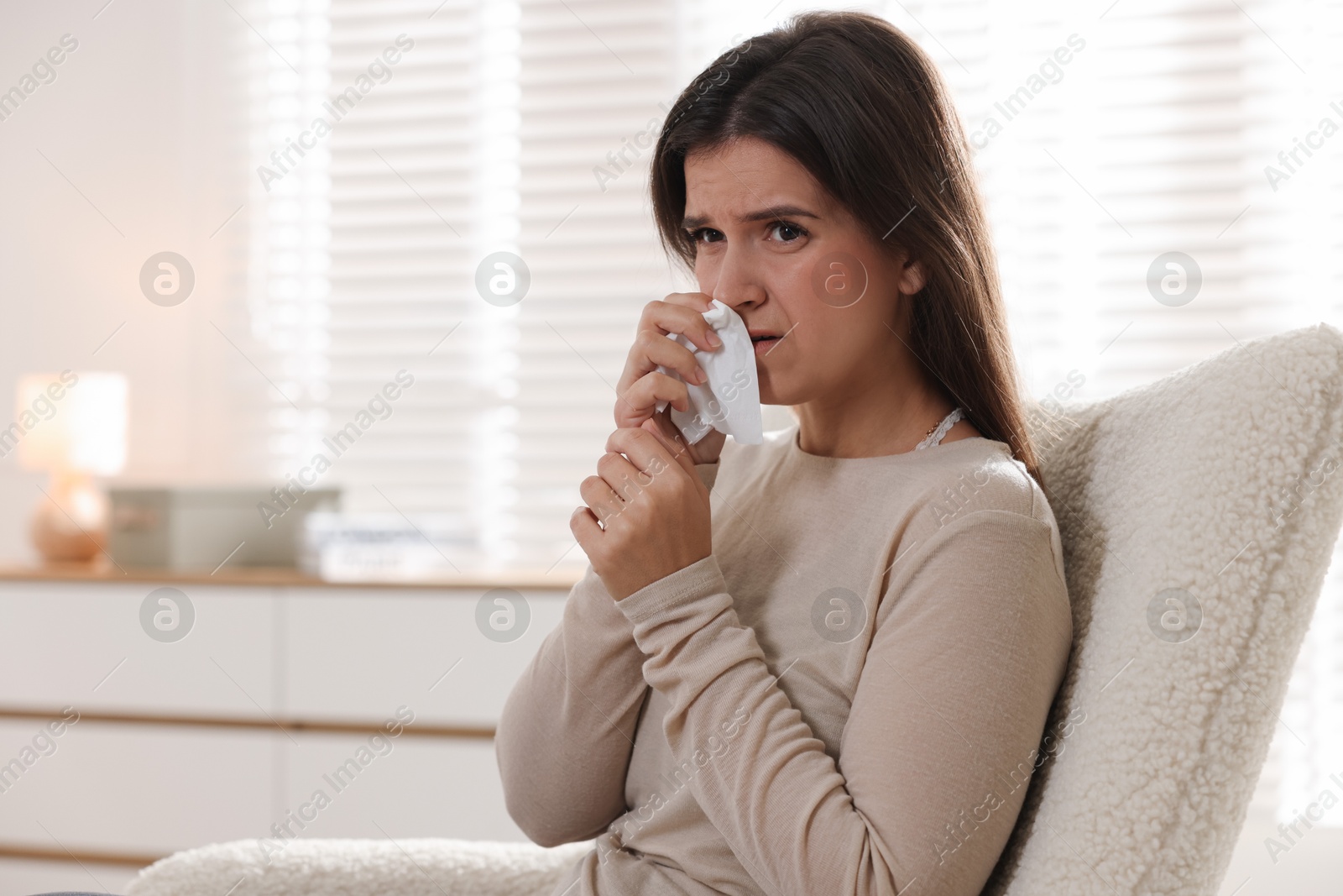 Photo of Young woman with tissue blowing runny nose at home. Space for text