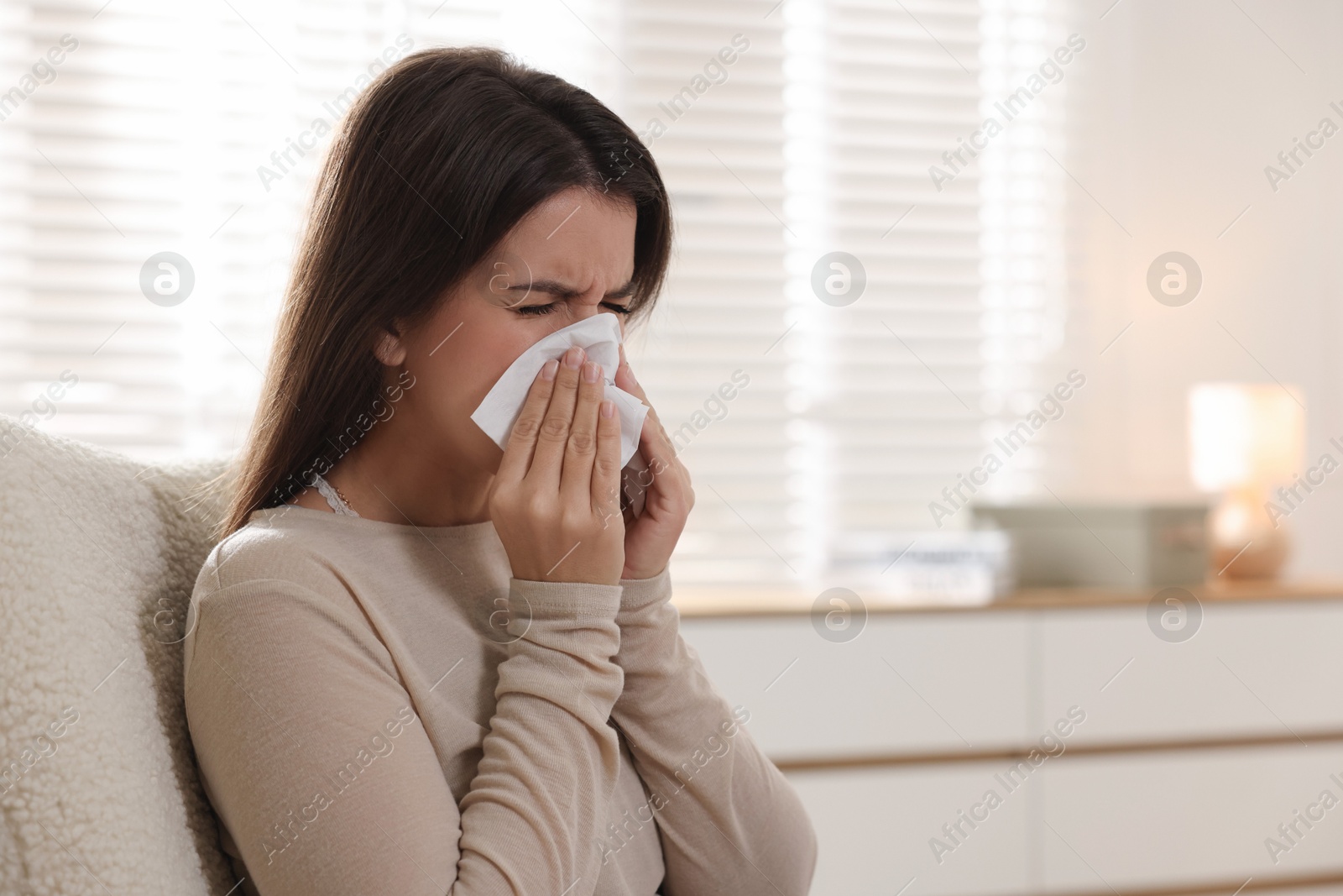 Photo of Young woman with tissue blowing runny nose at home. Space for text