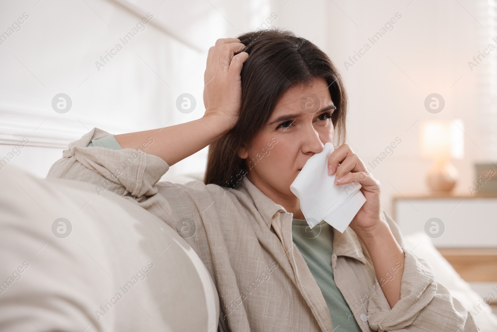 Photo of Young woman with tissue blowing runny nose at home