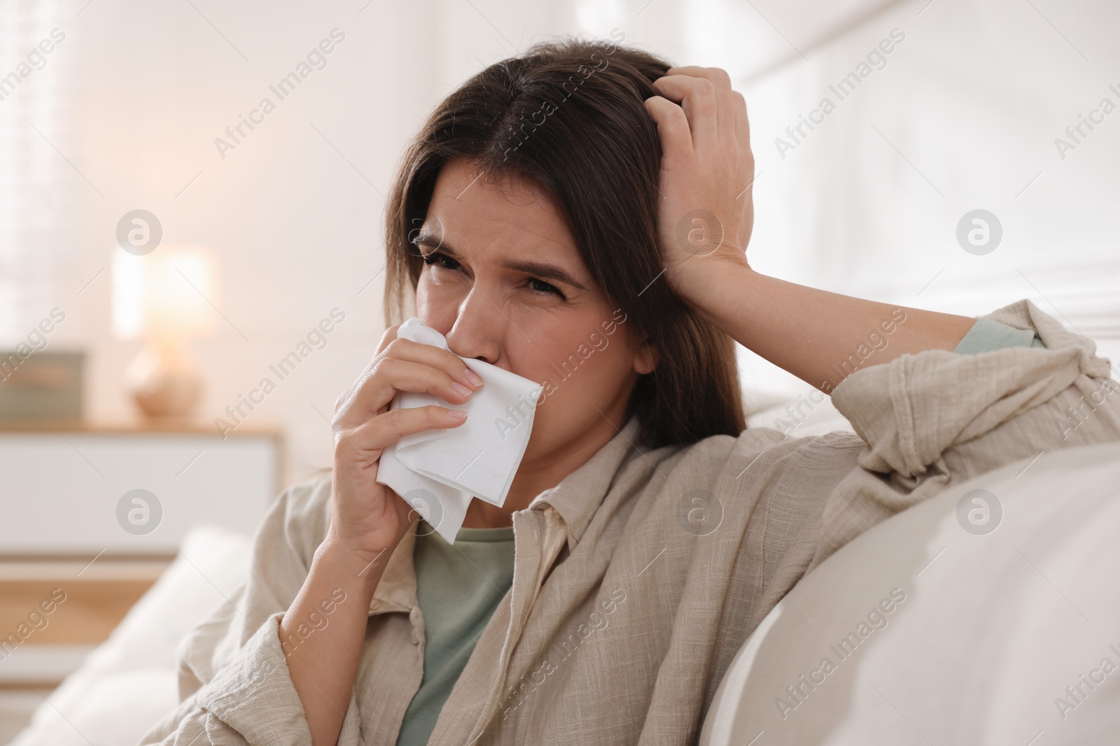 Photo of Young woman with tissue blowing runny nose at home