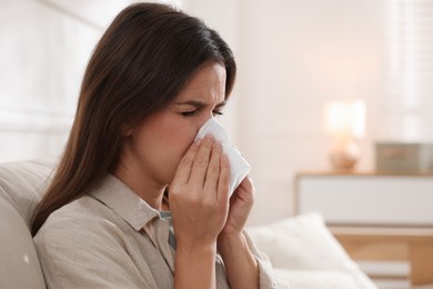 Young woman with tissue blowing runny nose at home