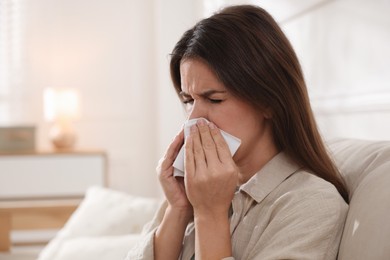 Young woman with tissue blowing runny nose at home