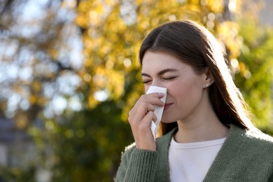 Woman with runny nose in park, space for text