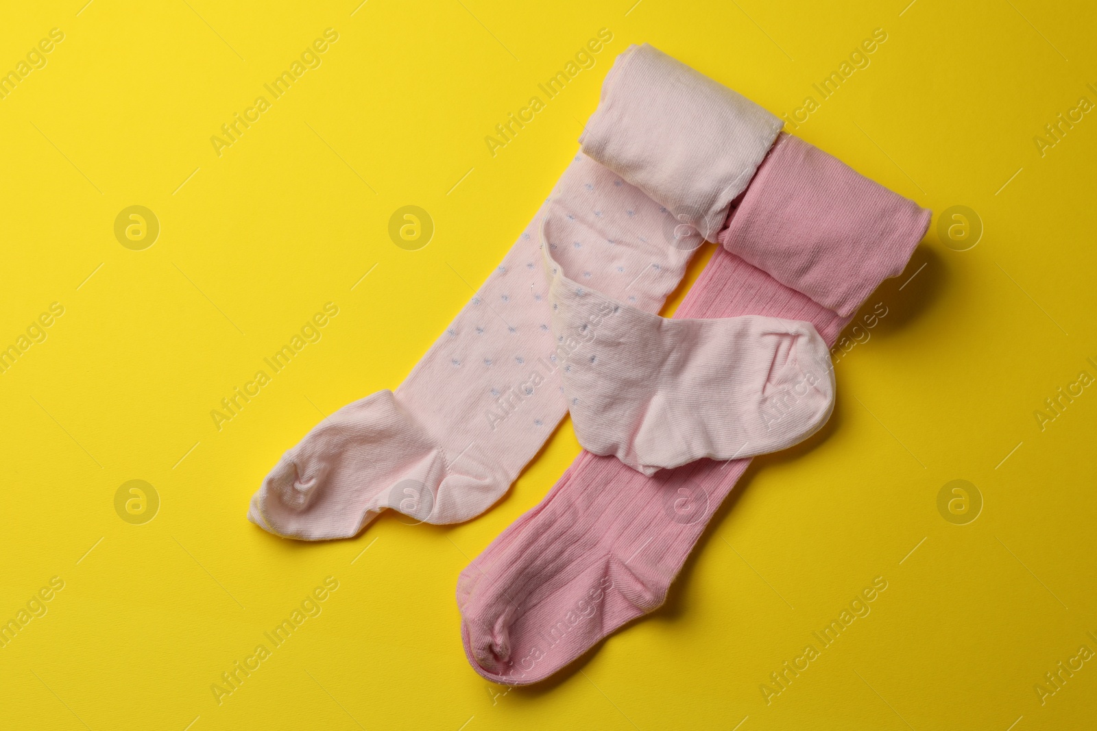 Photo of Pink child's tights on yellow background, top view