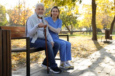 Photo of Caregiver assisting senior man on wooden bench in park, space for text. Home health care service