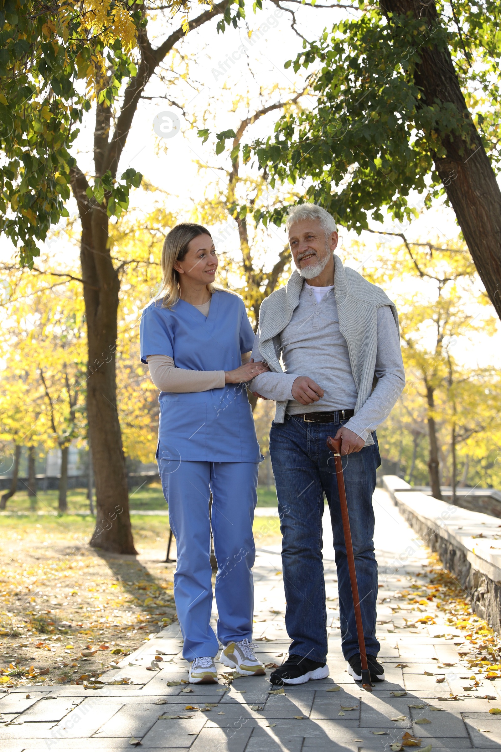 Photo of Caregiver assisting senior man in park. Home health care service