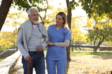 Photo of Caregiver assisting senior man in park, space for text. Home health care service