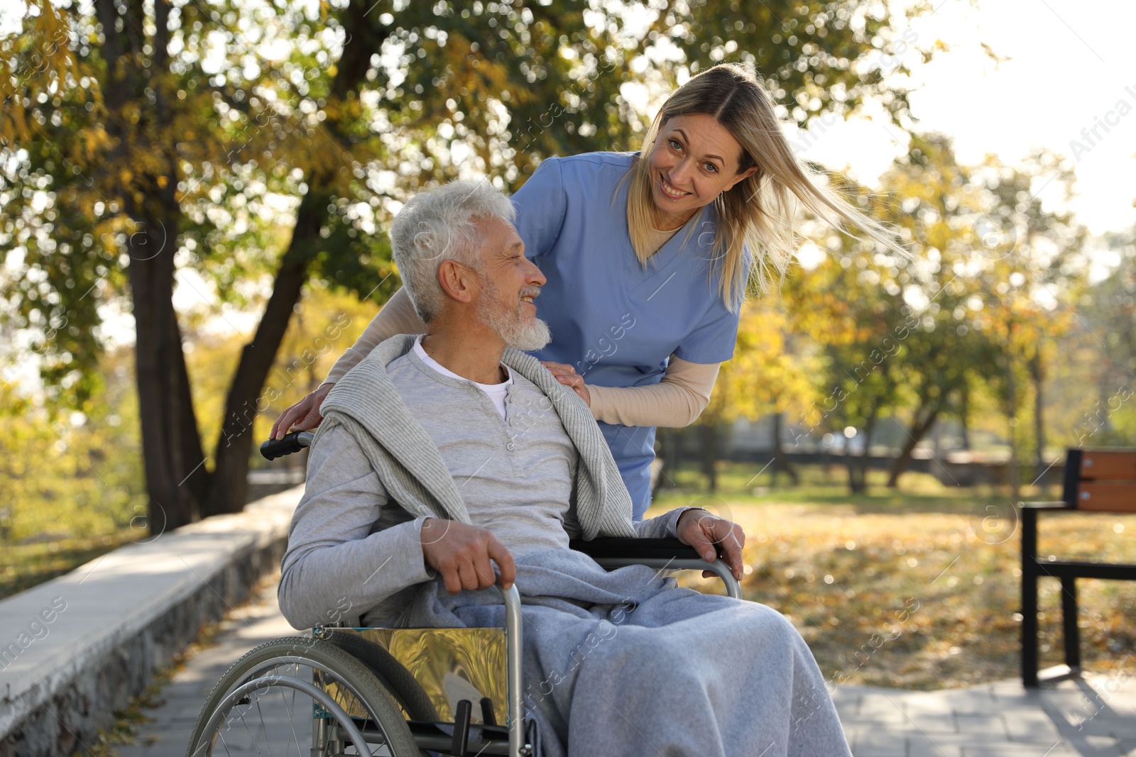 Photo of Caregiver assisting senior man on wheelchair in park. Home health care service