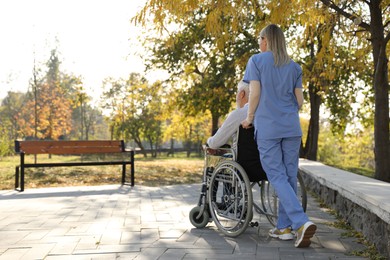 Photo of Caregiver assisting senior man on wheelchair in park, back view and space for text. Home health care service