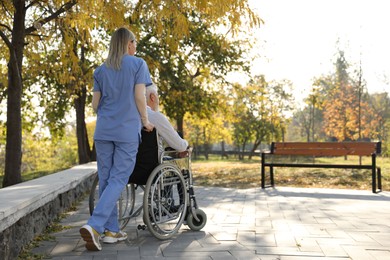 Photo of Caregiver assisting senior man on wheelchair in park, back view and space for text. Home health care service